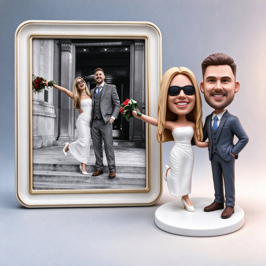 Framed wedding photo of a couple beside the custom wedding couple polymer clay figurine made from it, bride in white holding red roses