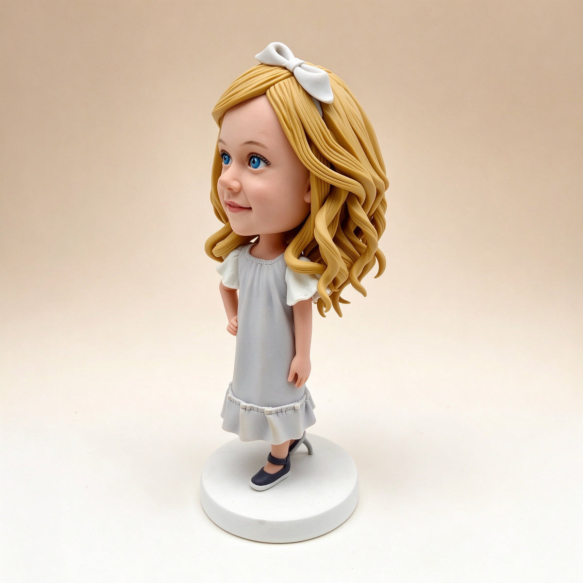 Side view of a handmade polymer clay bobblehead keepsake figurine of a girl with blonde hair and a white bow